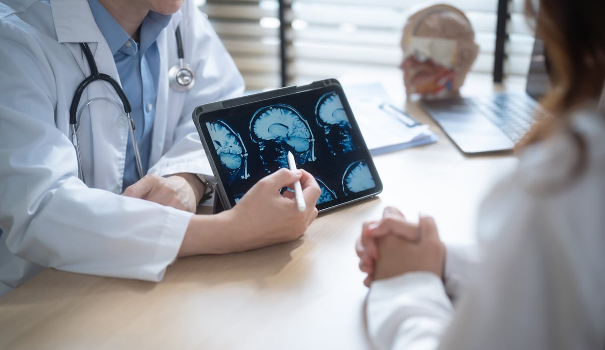 Close up of medical expert pointing at brain x-ray or MRI scan on tablet, explaining diagnosis and treatment plan to a patient in a clinic.
