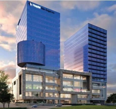 Modern mixed-use building complex with illuminated glass ground floor and two tall blue-tinted office towers at dusk