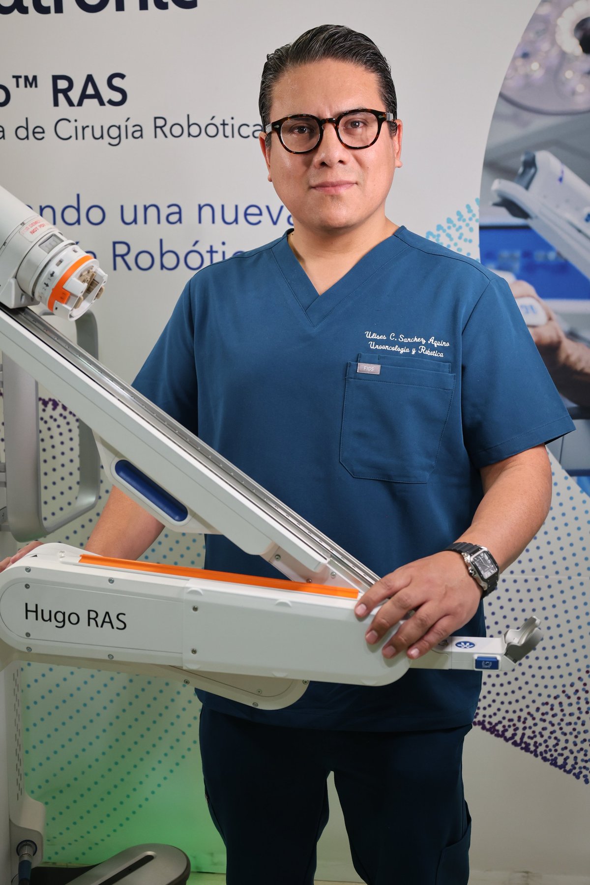 Male healthcare professional in blue scrubs holding robotic surgical equipment labeled Hugo RAS in a medical facility
