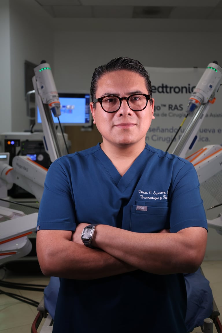 Male healthcare professional in blue scrubs and glasses standing with arms crossed in a medical office with ultrasound equipment in background