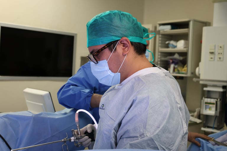 Surgeon in blue scrubs, mask, and surgical cap performing a procedure in a medical operating room