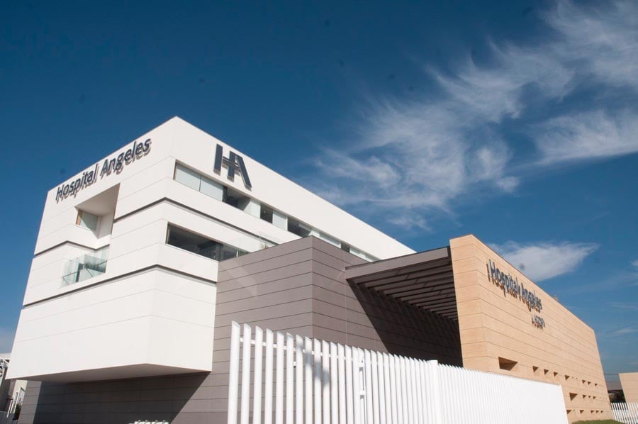 Modern building with white and tan facades featuring horizontal lines and large windows against a blue sky with clouds