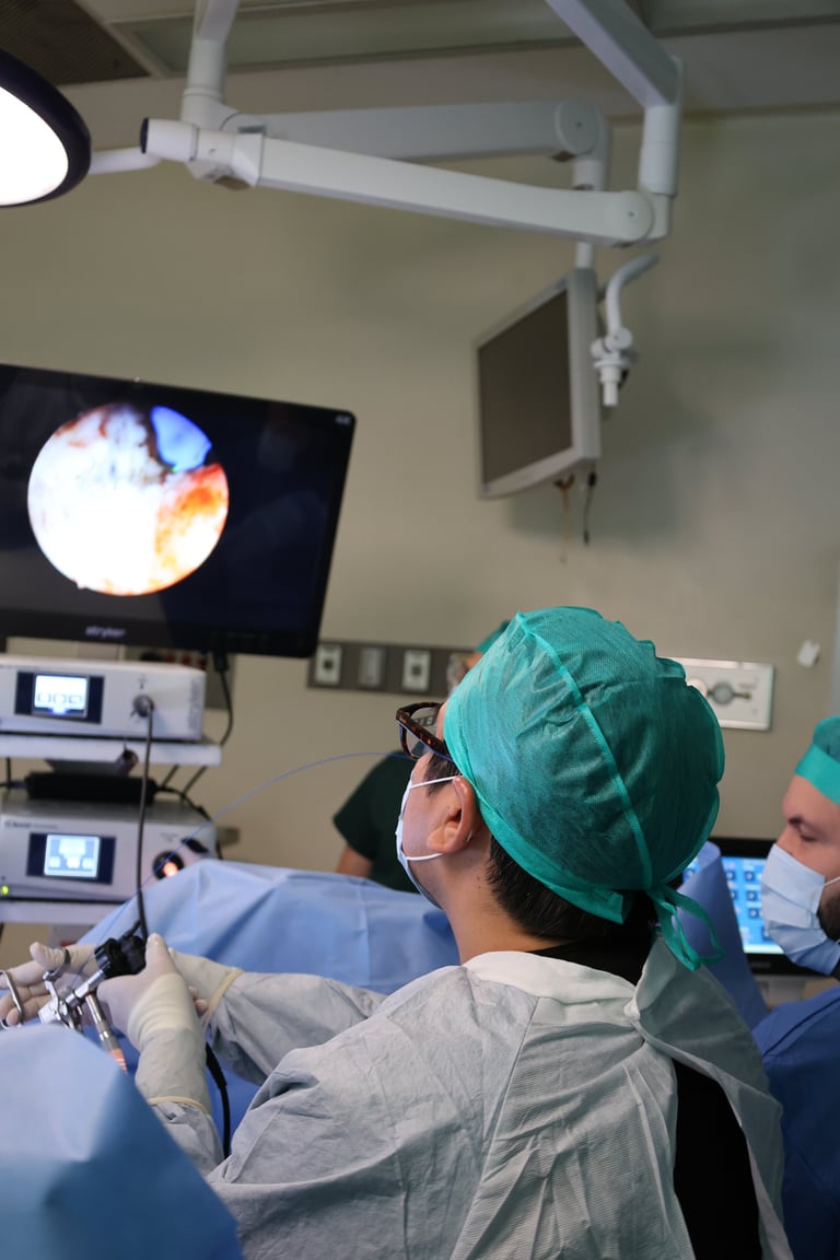 Surgical team in operating room wearing green surgical caps watching medical procedure on overhead monitor display