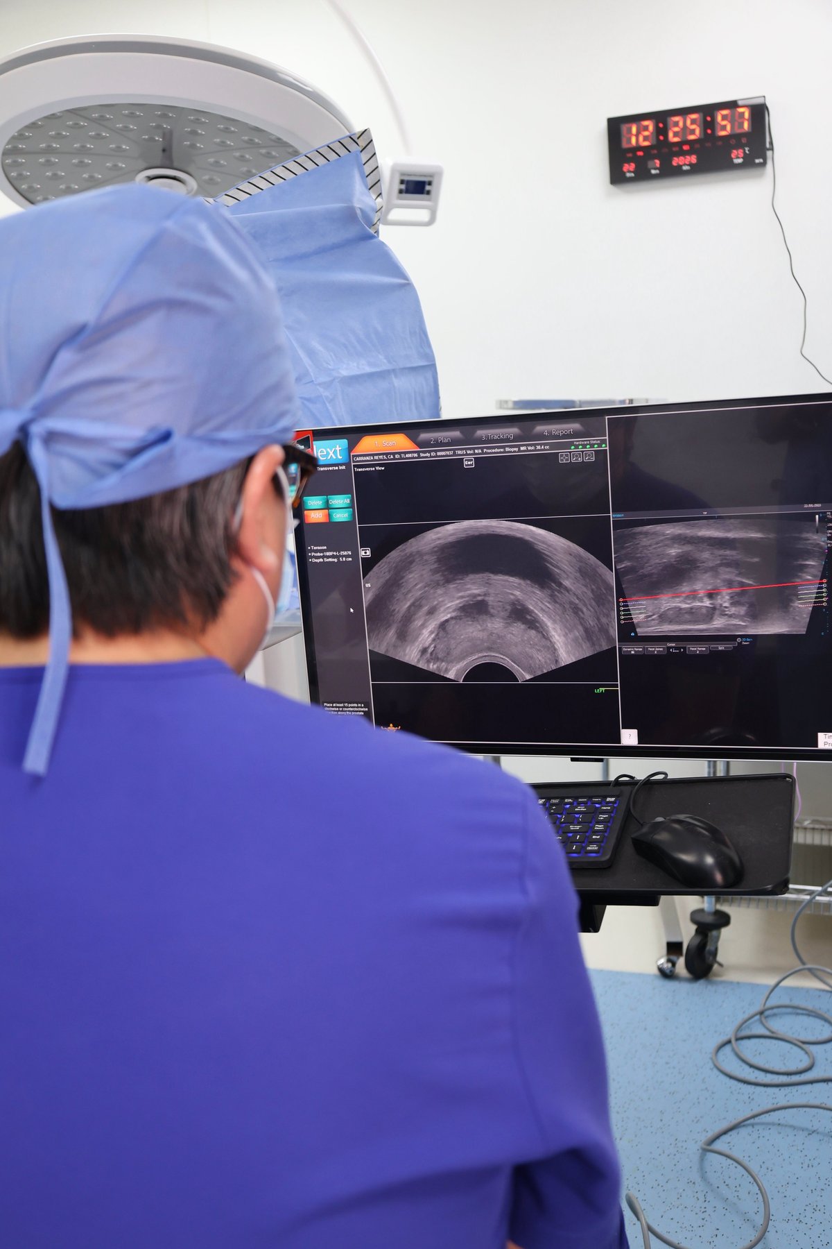 Surgeon in blue scrubs viewing ultrasound images on a monitor during a medical procedure in an operating room